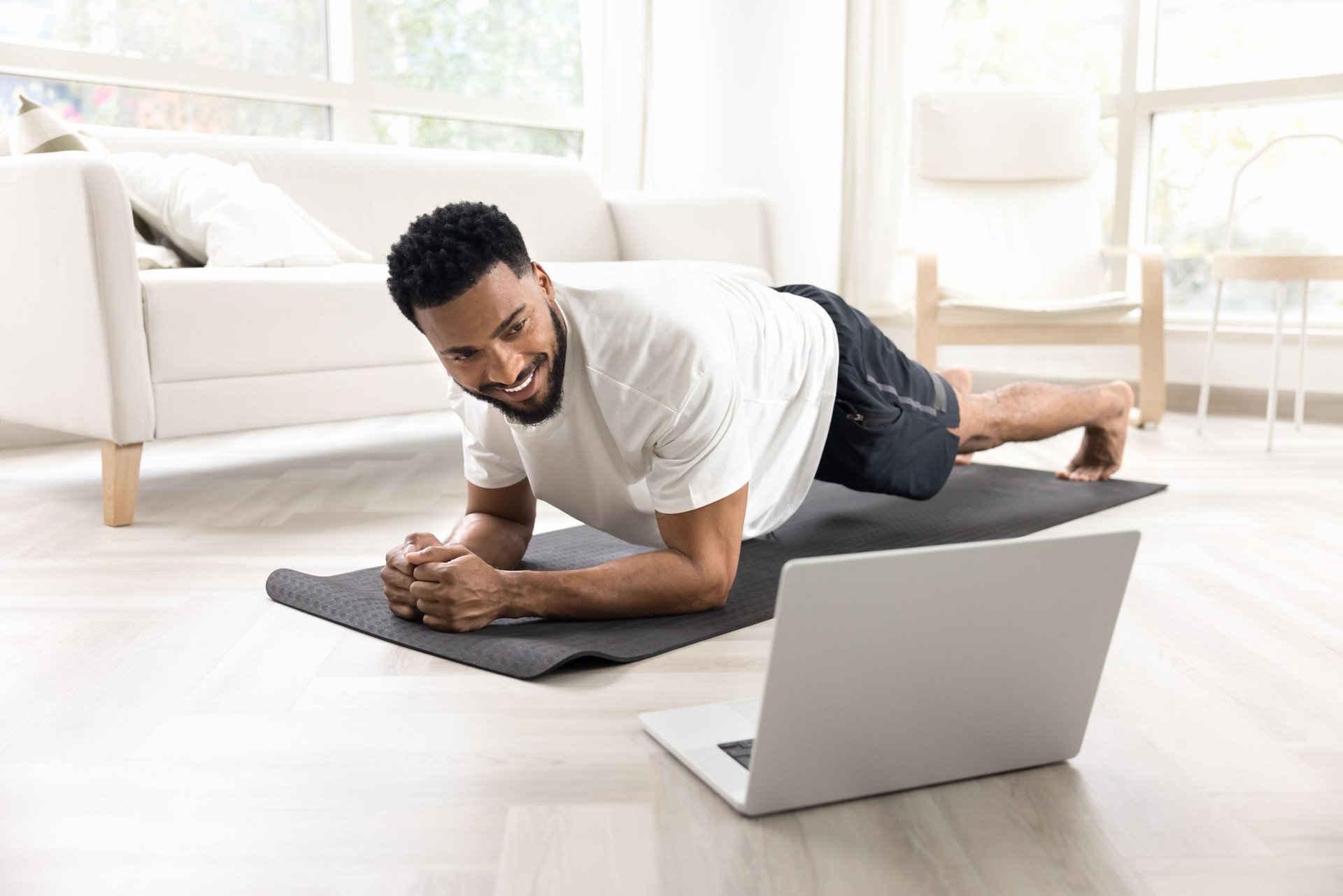 Cheerful strong African man keeping static plank on yoga mat