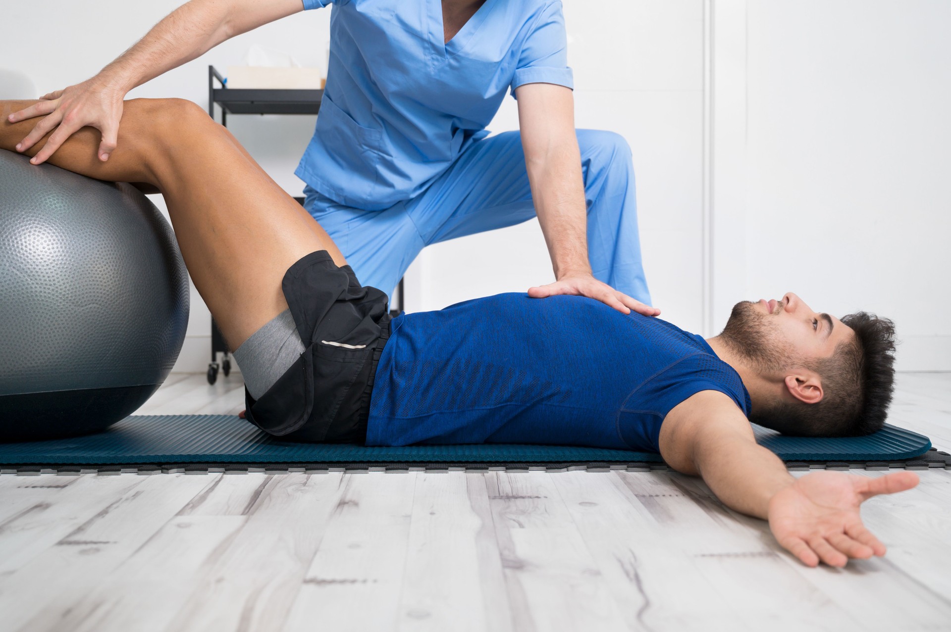 Physiotherapist helps handsome young patient with pilates exercises